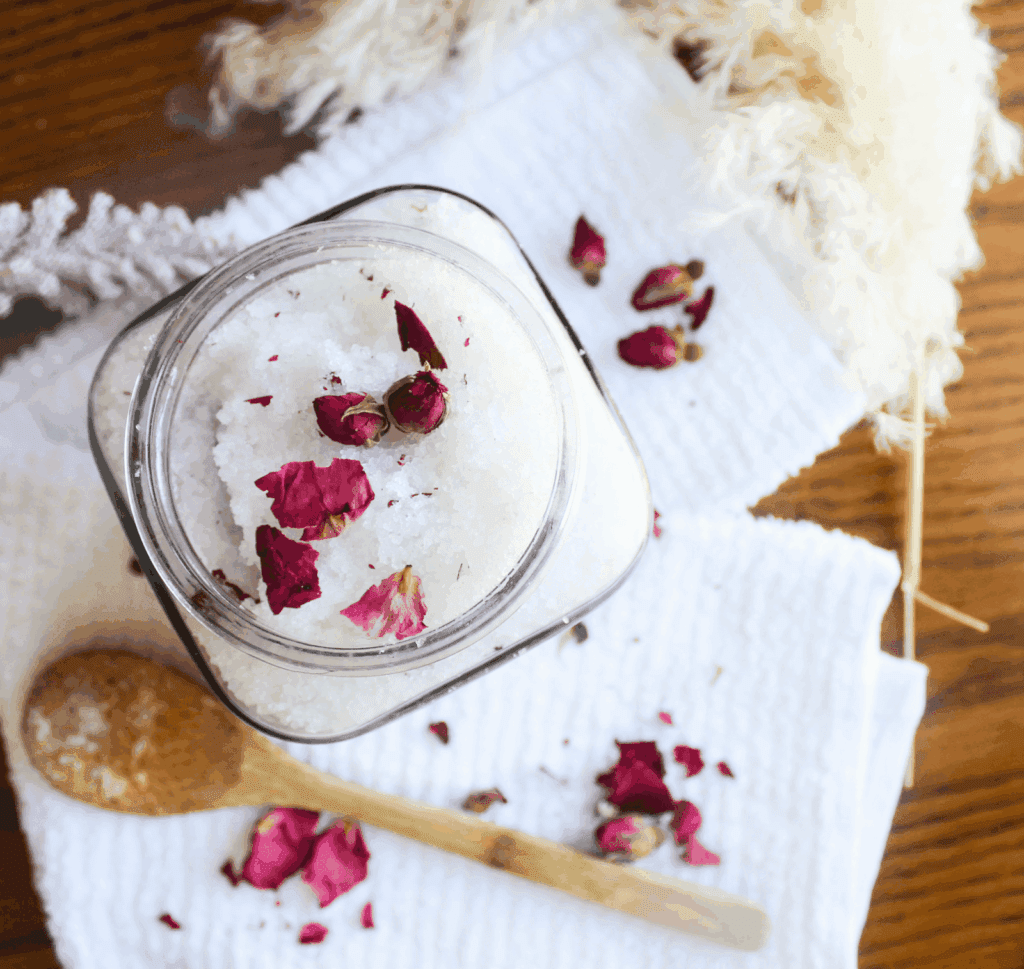 Glass jar filled with lavender rose bath salts topped with dried rose petals