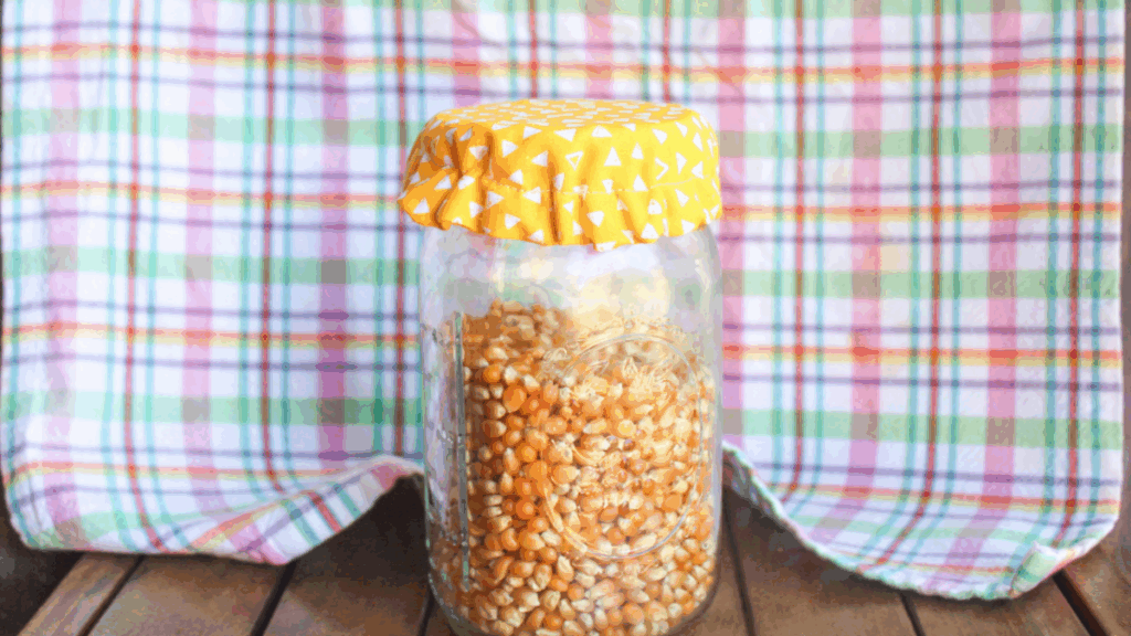 Mason jar with a handmade yellow fabric cover featuring white triangles, sitting on a wooden surface