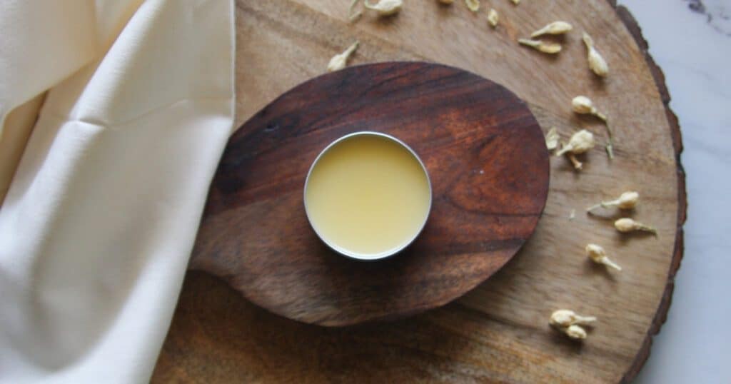 Homemade lip balm in a silver tin, placed next to cream-colored fabric.