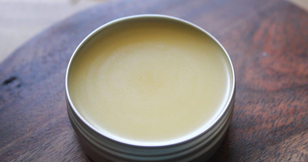 Finished homemade tallow lip balm in a silver tin on a wood background.