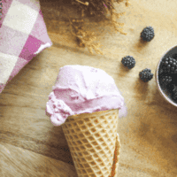 Blackberry ice cream in a waffle cone held outdoors with a rustic background