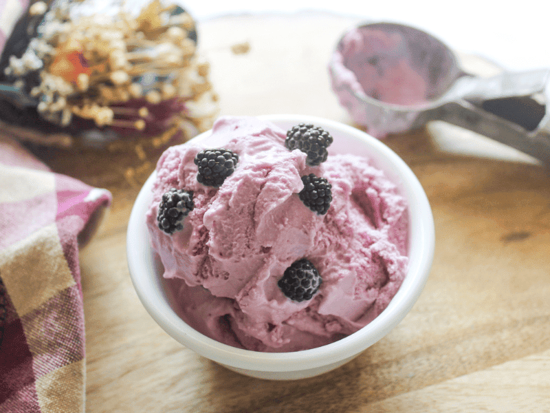 Scoop of blackberry ice cream in a white bowl with spoon
