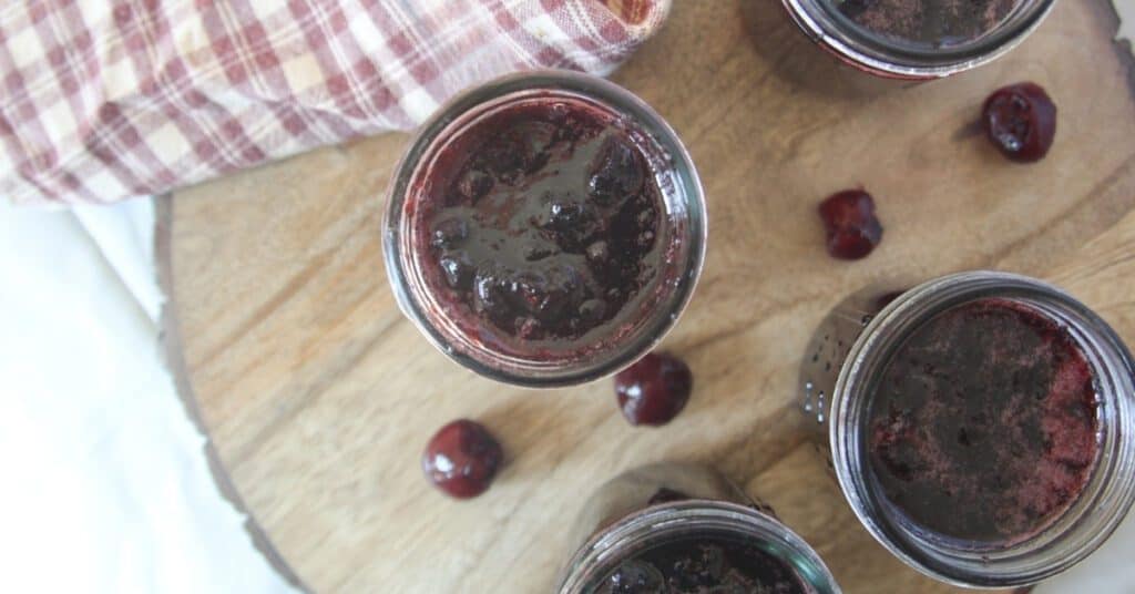 Open glass jars filled with homemade cherry jam on a wooden surface.