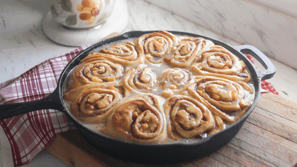 Fully glazed peach cinnamon rolls in a black skillet, ready to serve.