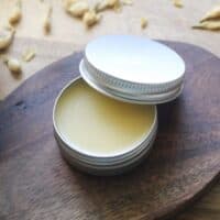 DIY tallow lip balm tin with lid propped open, surrounded by dried jasmine flowers.