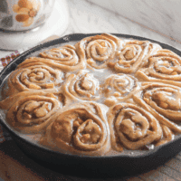 Fully glazed peach cinnamon rolls in a black skillet, ready to serve.