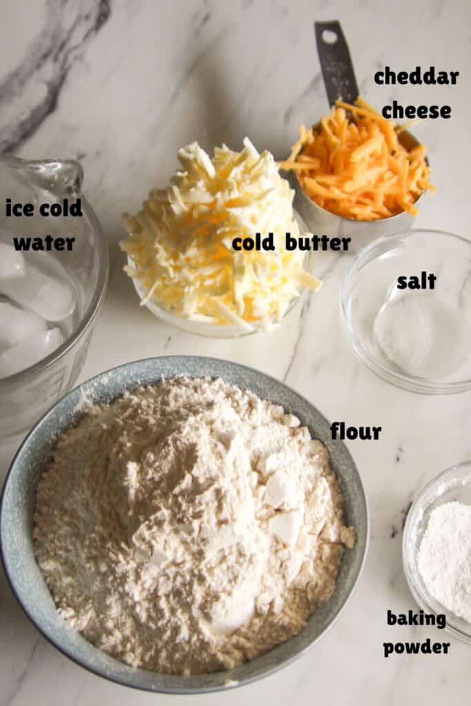 Easy Cheddar Biscuits All ingredients for homemade cheddar biscuits laid out in bowls on a countertop.