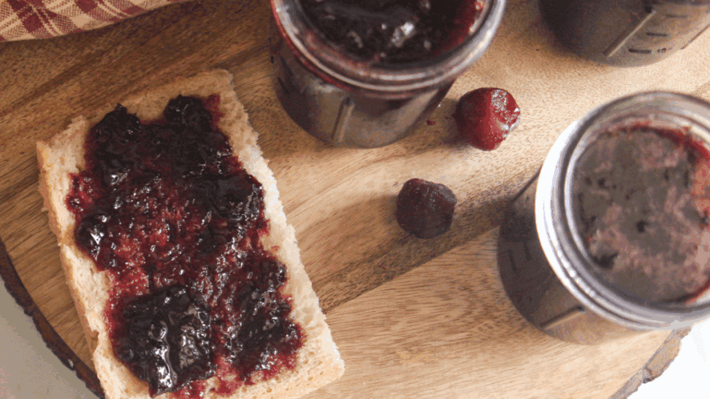 Slice of toast topped with cherry jam next to filled mason jars