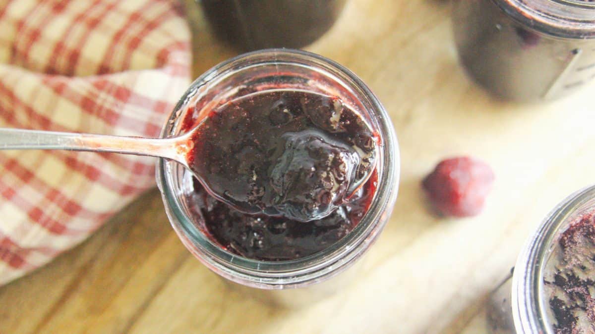 Spoonful of homemade cherry jam held above an open jar