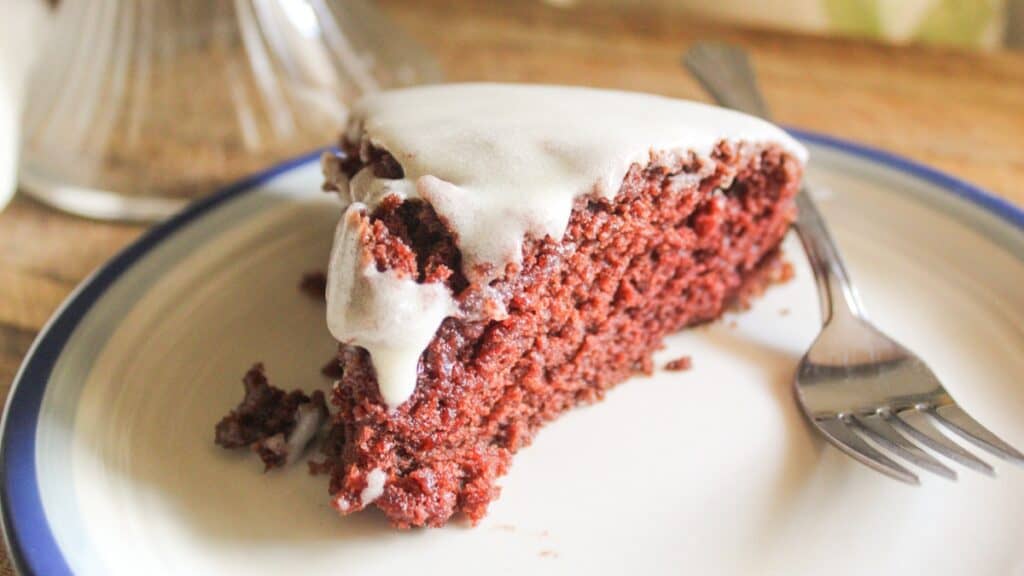 A close-up head-on view of a single slice of chocolate cake with white icing on a plate.