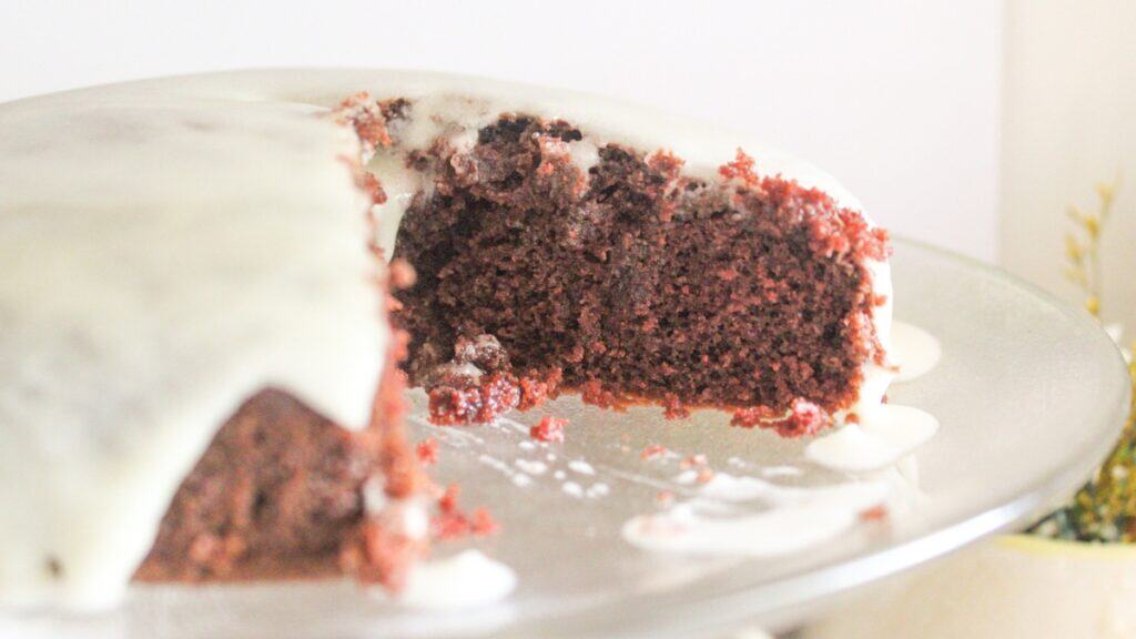 A whole chocolate cake with white icing, displayed on a stand with one slice removed.