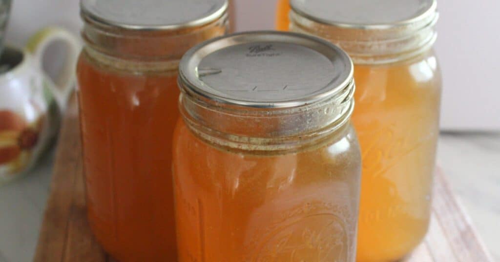 Close-up of golden bone broth in three mason jars on a rustic wood counter