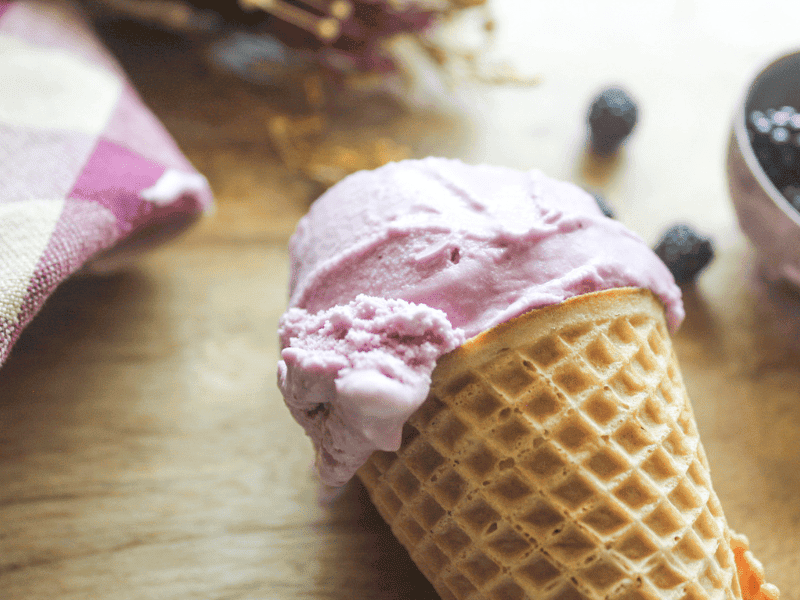 Creamy homemade blackberry ice cream melting slightly in a waffle cone