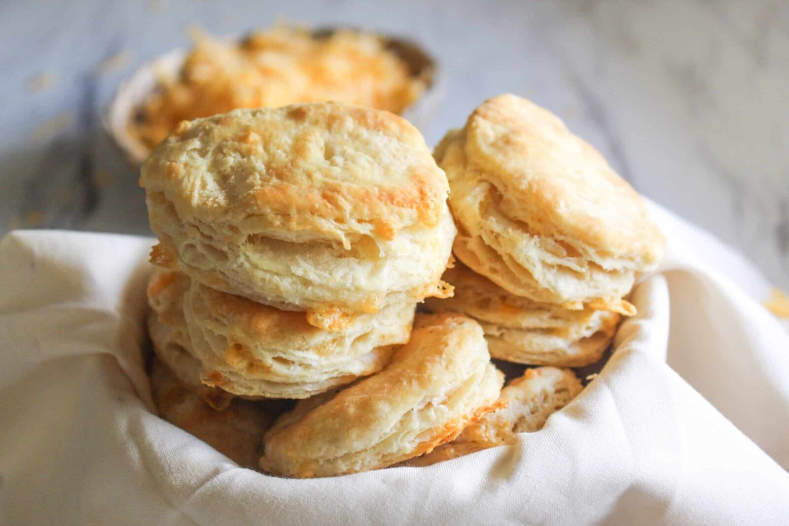 Easy Cheddar Biscuits Stack of golden homemade cheddar biscuits on a rustic wooden board, showing flaky layers and melted cheese.
