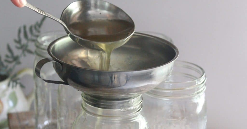 Freshly made chicken bone broth being poured into a mason jar through a strainer.