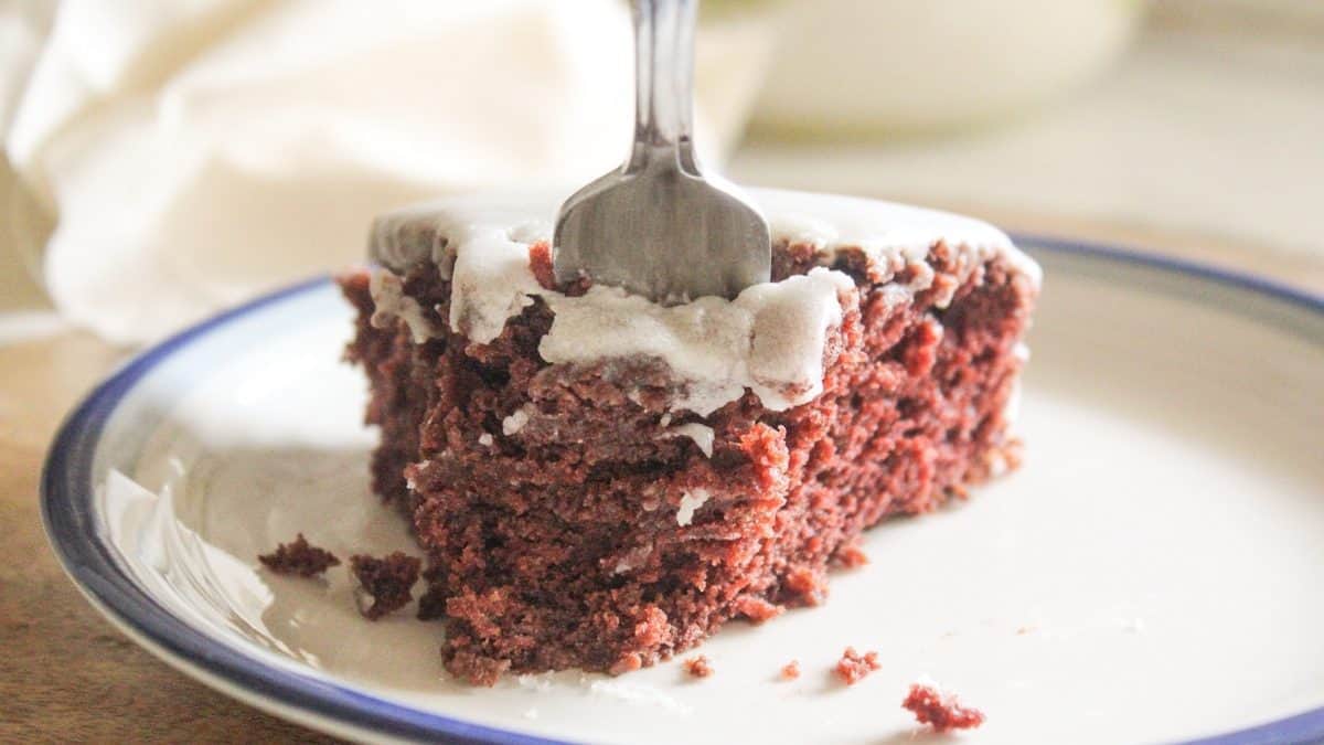 A close-up of a slice of chocolate cake with white icing, a fork pressing into the soft crumb.