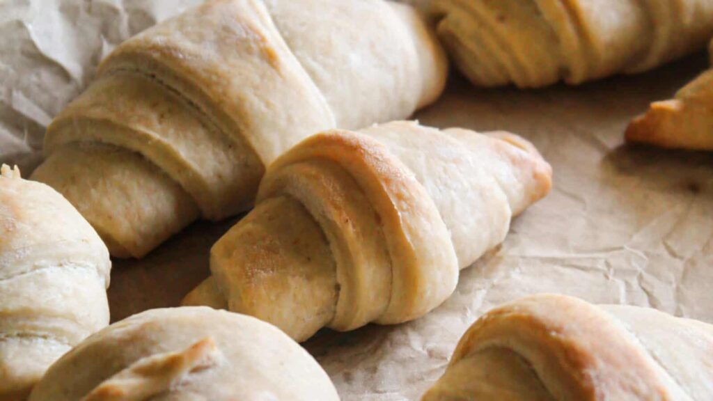 Baked sourdough crescent rolls cooling on parchment paper