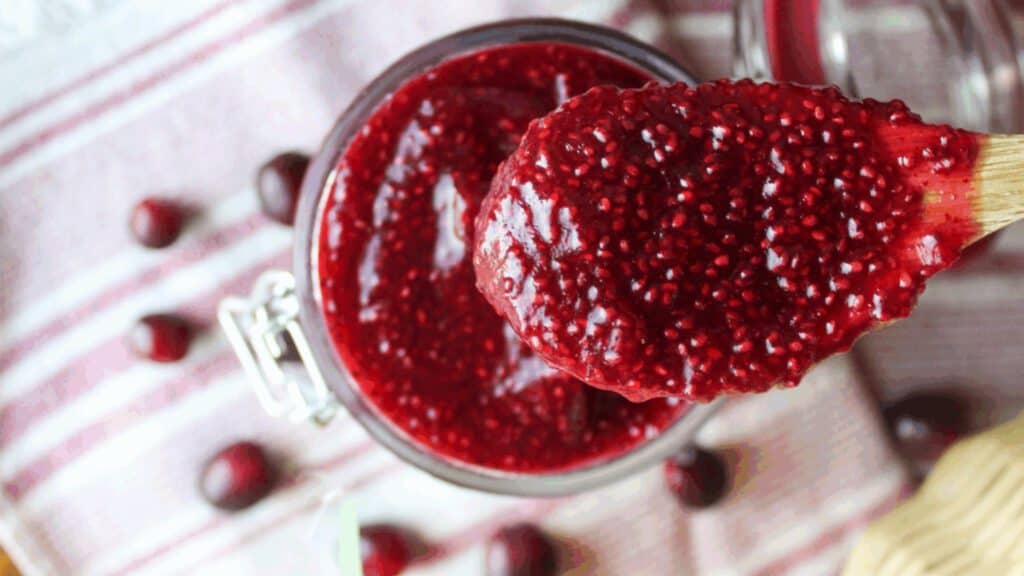 Close-up of homemade cranberry chia jam in a glass jar, showing its thick texture and vibrant red color.