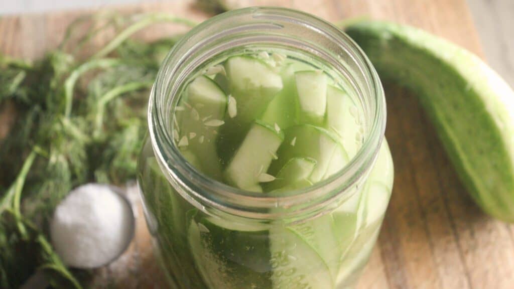 Close‑up of a glass jar filled with fermented dill pickles and fresh herbs.