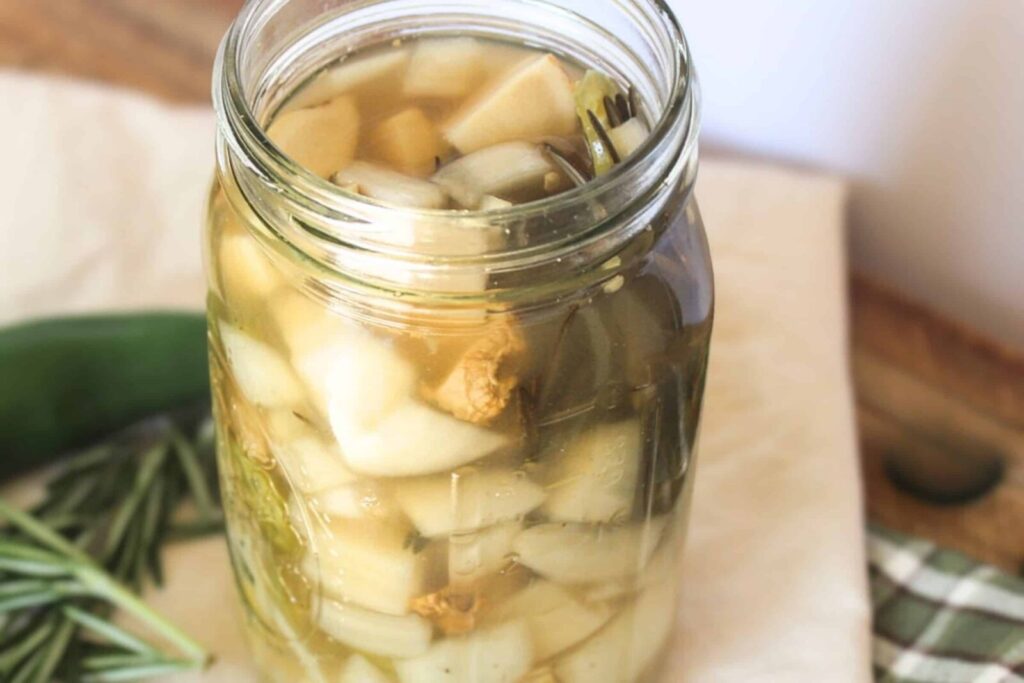 Homemade fire cider recipe in a glass jar with fresh ginger, garlic, and jalapeño.
