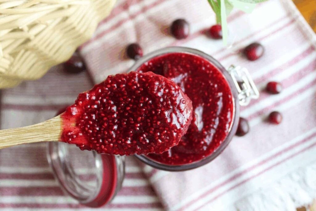 Cranberry Chia Jam A spoonful of healthy cranberry chia jam being scooped from a jar, showcasing its rich color and jammy consistency.