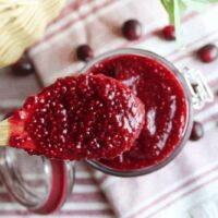 A spoonful of healthy cranberry chia jam being scooped from a jar, showcasing its rich color and jammy consistency.