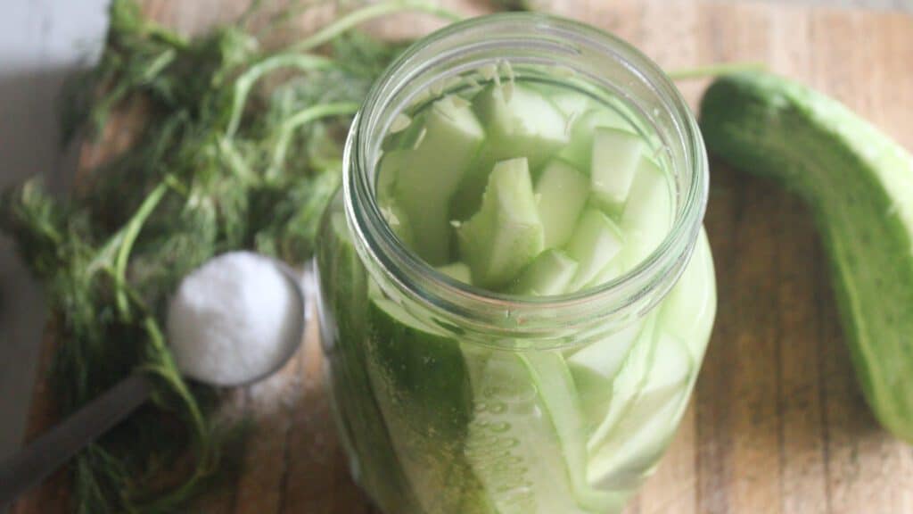 Old‑fashioned fermented dill pickles in a glass jar with brine and herbs.