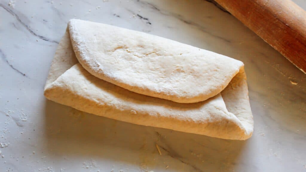 Rolling and folding sourdough dough into layers for flaky crescent rolls