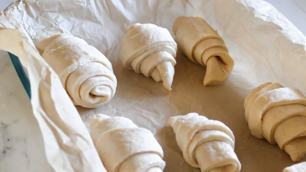 Shaped sourdough crescent rolls rising on parchment paper