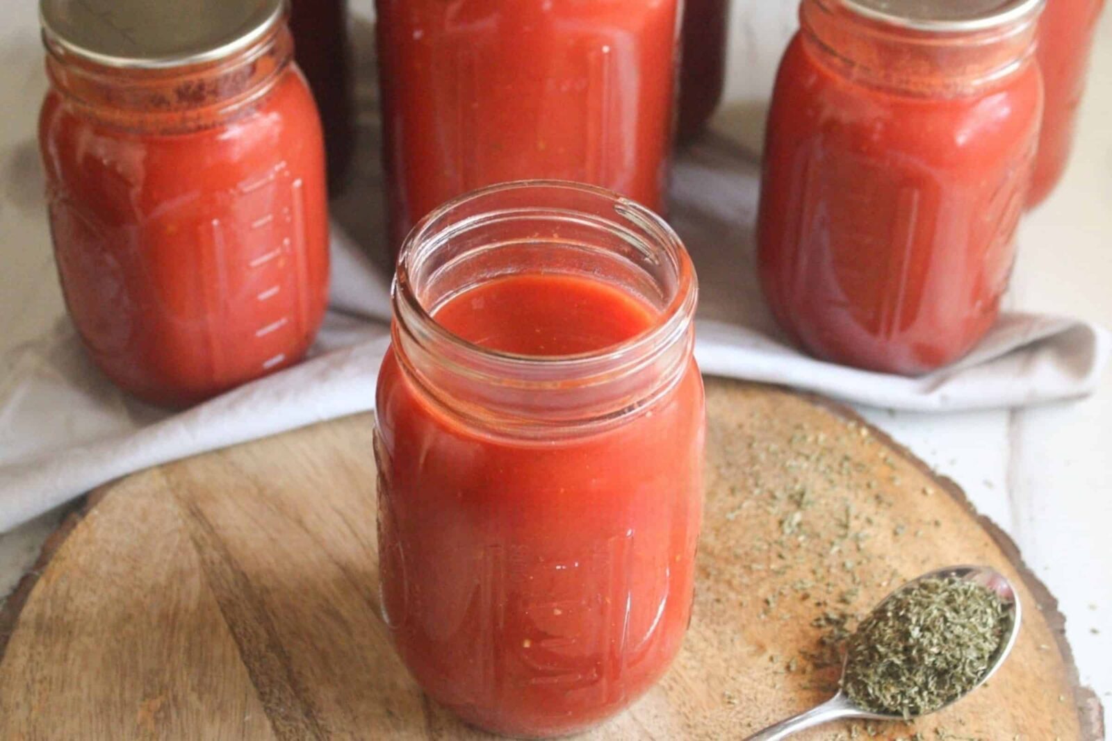Open jar of roasted tomato sauce on a wooden board with sealed jars behind it, made using water bath canning