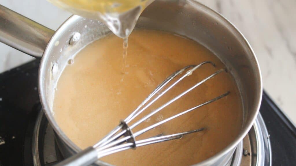 Bone Broth Gravy Pouring bone broth into a saucepan while whisking gravy.