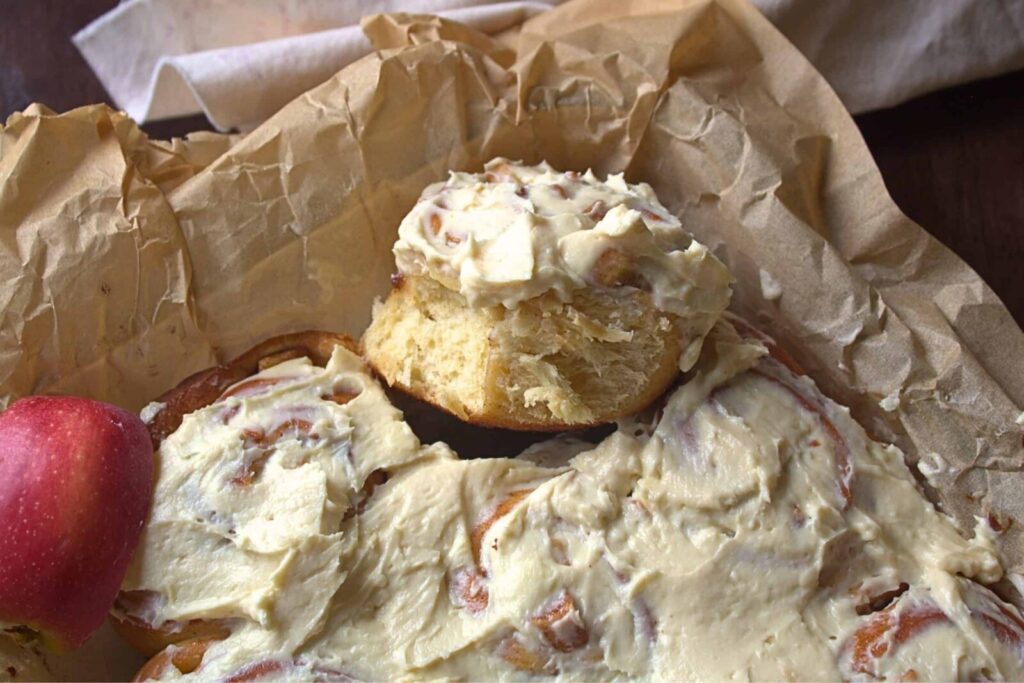 Homemade apple pie cinnamon rolls with honey cream cheese frosting on parchment paper.