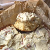 Apple Pie Cinnamon Rolls Homemade apple pie cinnamon rolls with honey cream cheese frosting on parchment paper.