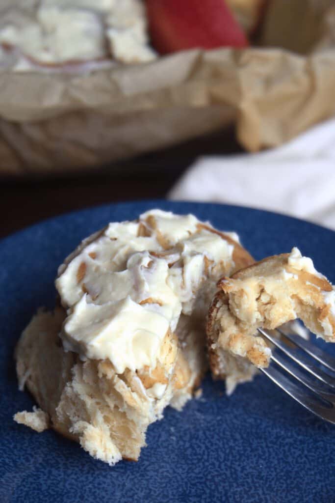 Apple Pie Cinnamon Rolls Close-up of a frosted apple pie cinnamon roll with a forkful on a blue plate