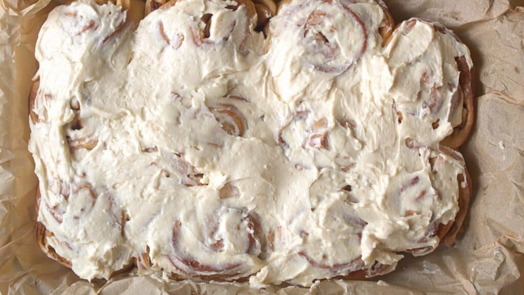 Apple Pie Cinnamon Rolls Pan of baked apple pie cinnamon rolls covered in cream cheese frosting.