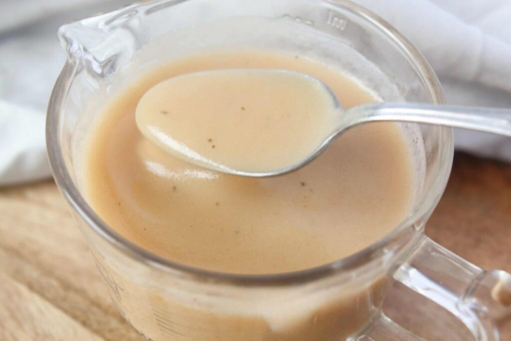 Creamy homemade bone broth gravy in a glass measuring cup with a spoon.