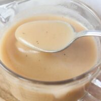 Bone Broth Gravy Creamy homemade bone broth gravy in a glass measuring cup with a spoon.