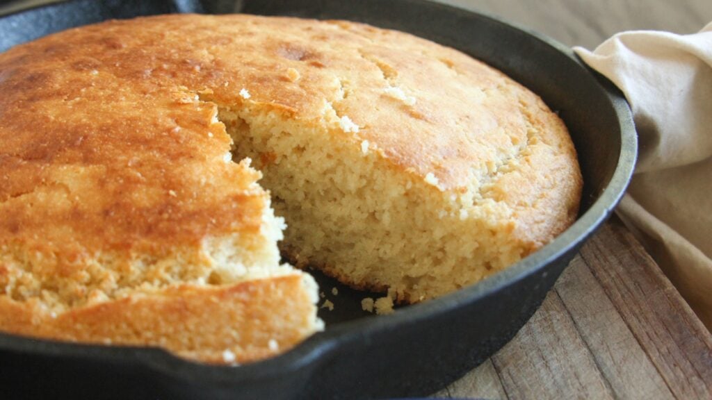 Honey cornbread in cast iron skillet with a wedge cut out.
