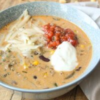 Creamy taco soup in a blue bowl topped with shredded cheese, salsa, and sour cream.