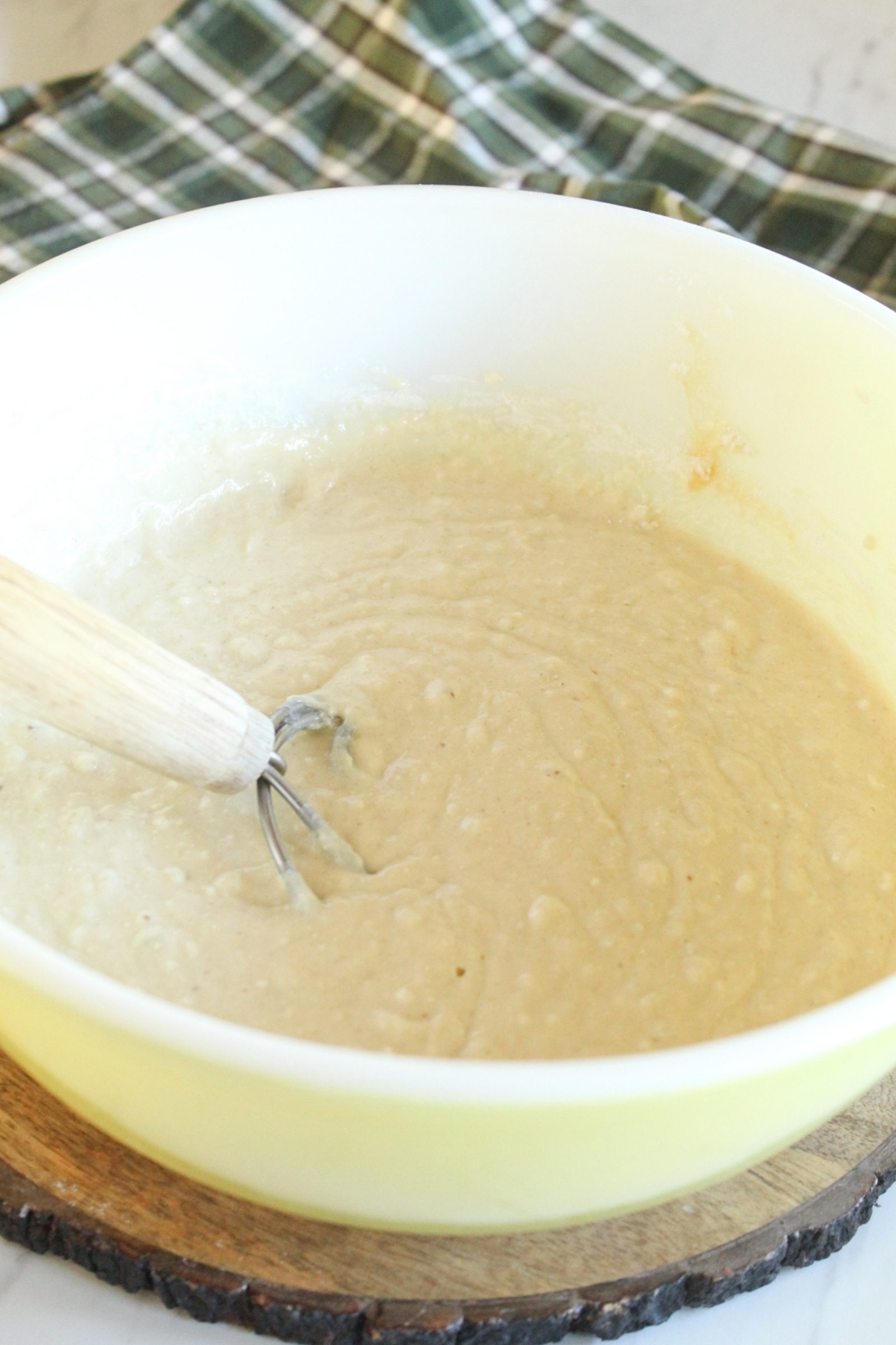 Honey cornbread batter in a mixing bowl with whisk on rustic wood trivet.