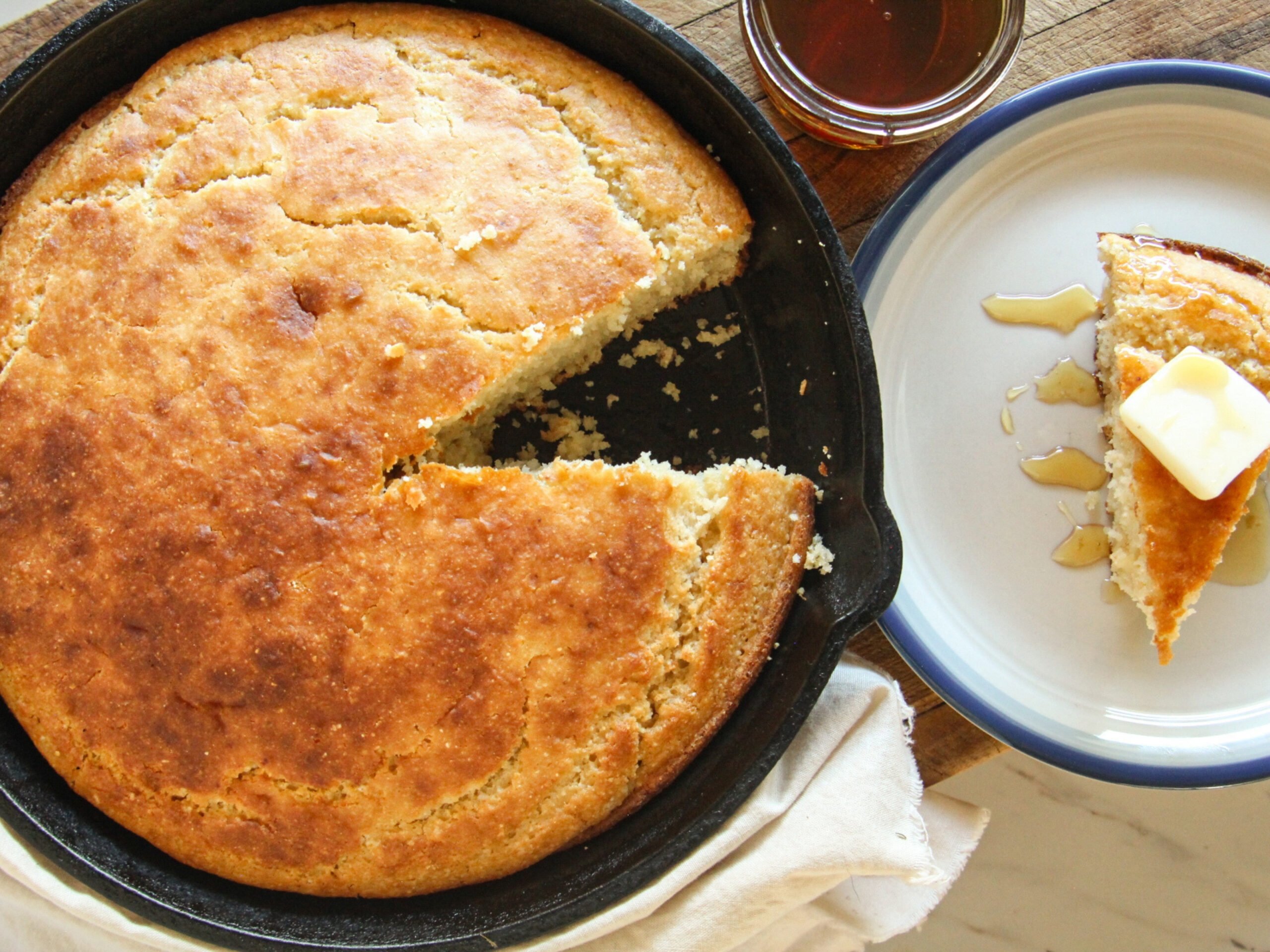 Golden honey cornbread baked in a cast iron skillet with one slice cut out.