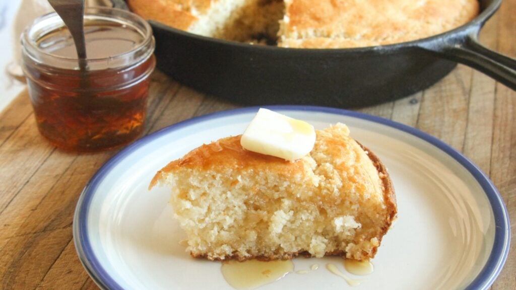 Slice of honey cornbread on a plate with melting butter and honey drizzle.