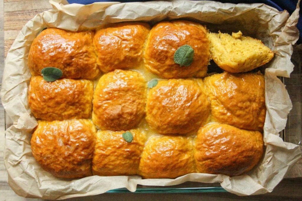 Freshly baked golden pumpkin dinner rolls in a parchment-lined pan.