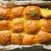 Freshly baked golden pumpkin dinner rolls in a parchment-lined pan.
