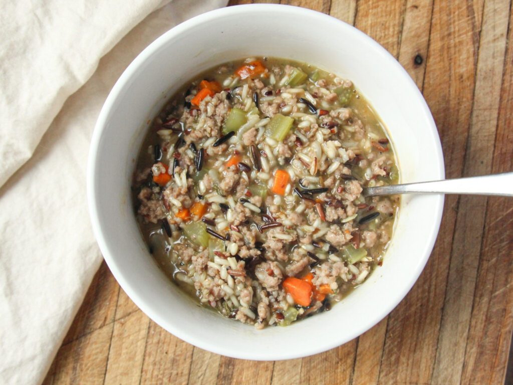 Bowl of homemade sausage wild rice soup with carrots, celery, and bone broth on a wooden table.