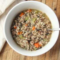 Bowl of homemade sausage wild rice soup with carrots, celery, and bone broth on a wooden table.