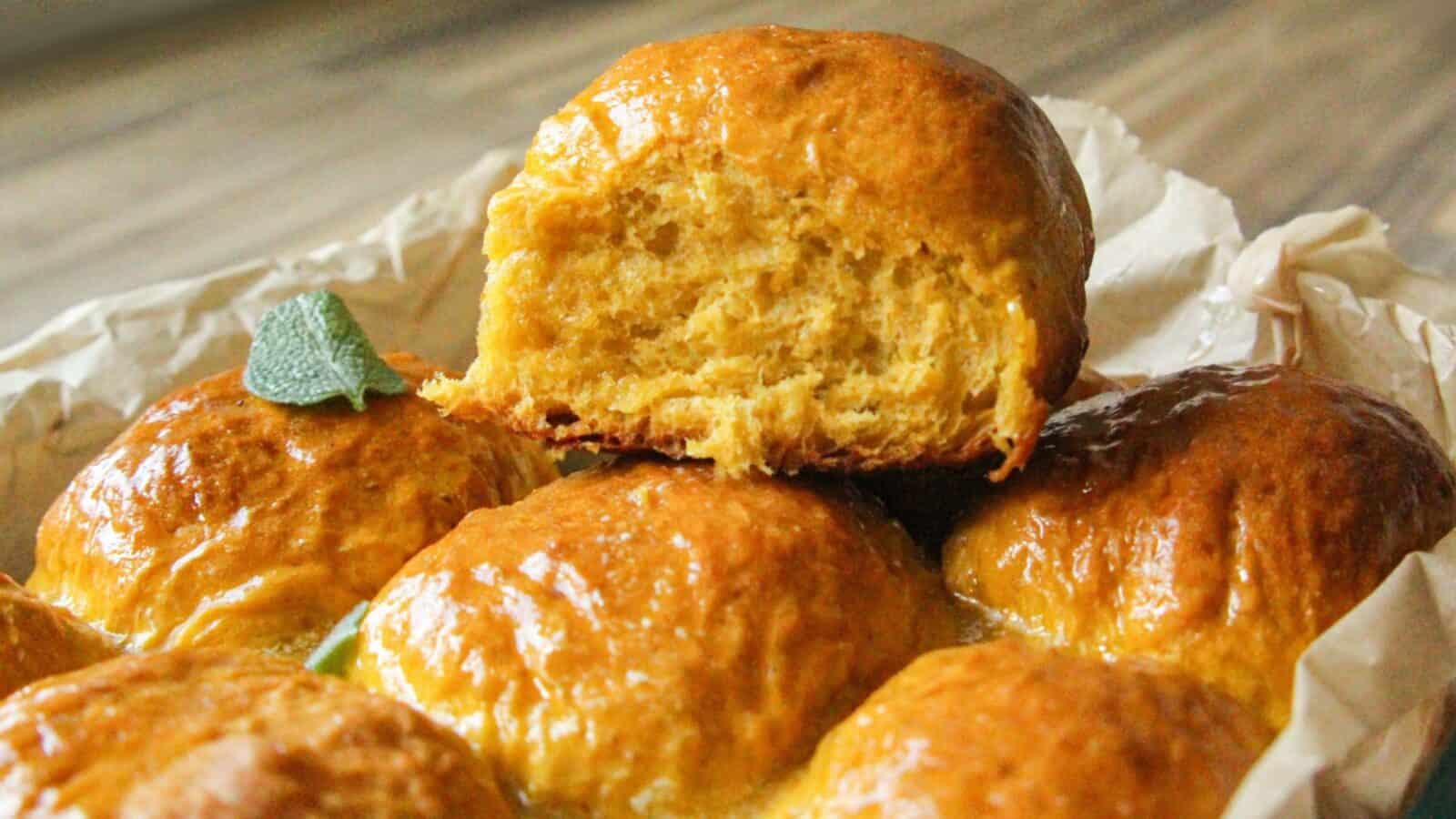 Close-up of a golden brown pumpkin dinner roll with sage leaf.