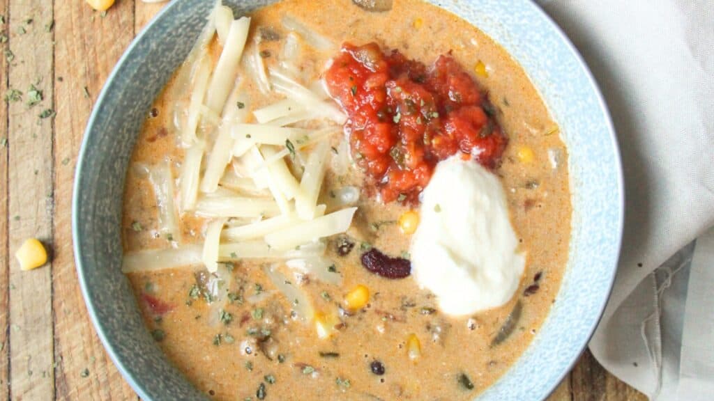 Overhead view of creamy taco soup with beans, corn, salsa, cheese, and sour cream.