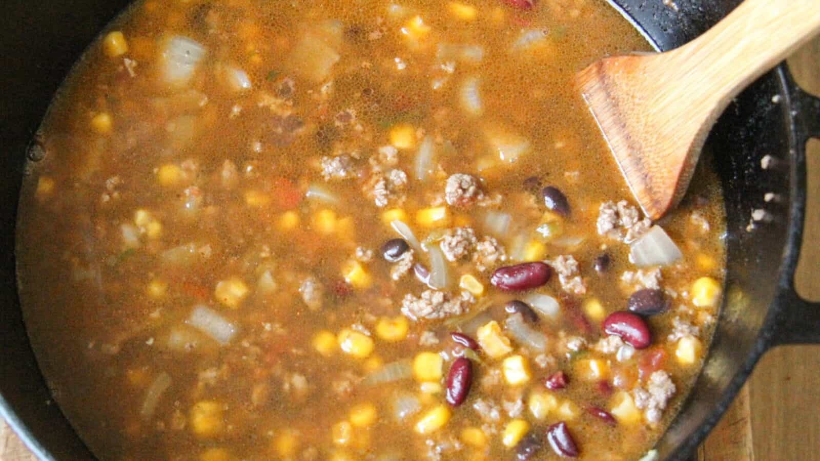 Taco soup simmering in a pot with ground beef, beans, corn, and onions.