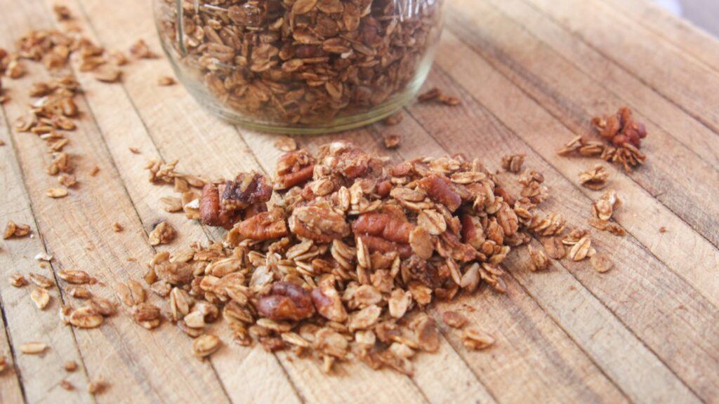 Homemade pecan pie granola on a wooden cutting board with a glass jar of granola in the background.